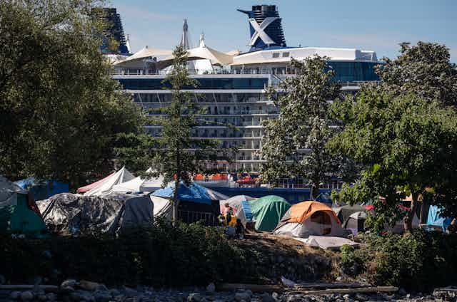 A group of tents in a park. A large cruise ship passes behind.