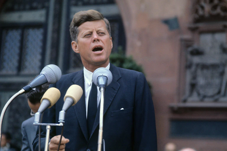 John F Kennedy debout devant des microphones.
