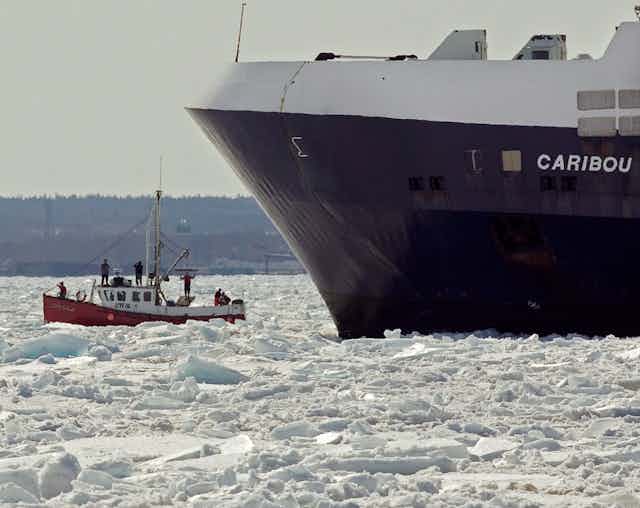 A small sealing boat beside a much larger boat and surrounded by ice.