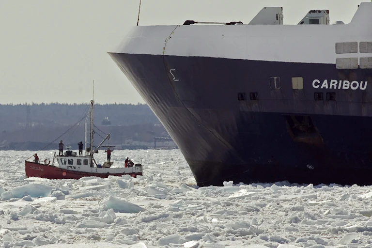 A small sealing boat beside a much larger boat and surrounded by ice.