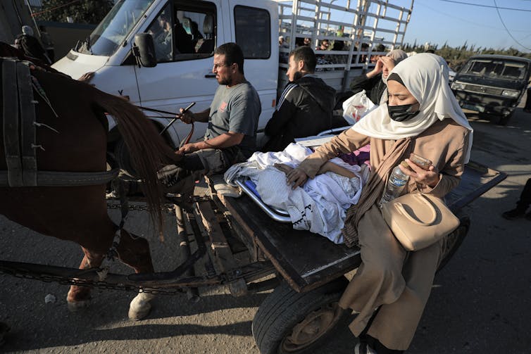 Une femme en robe et foulard accompagne un patient sur une civière.