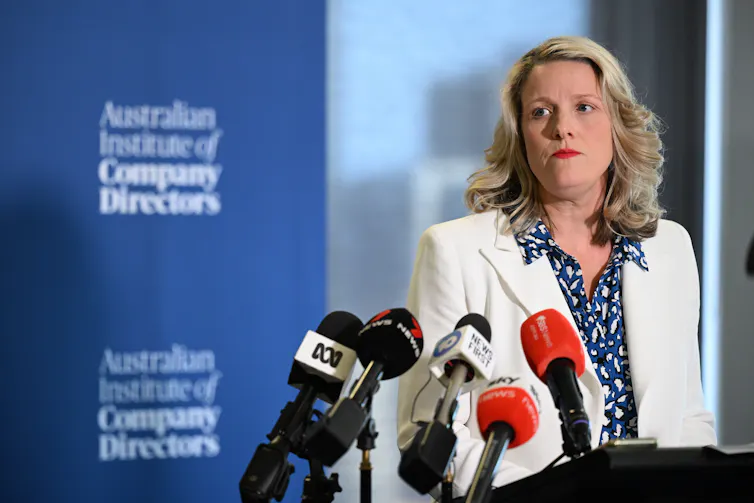 A blonde woman in a white blazer addresses a media conference