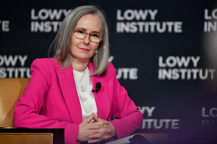 A woman in a bright print blazer sits and looks to an audience