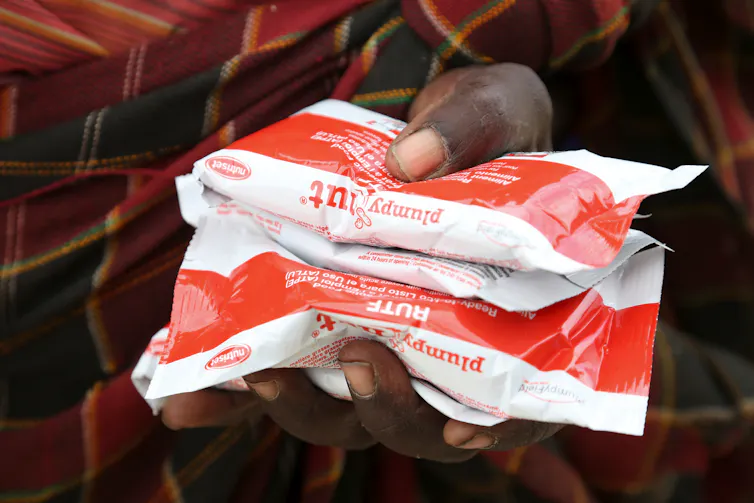 A hand holding packets of Plumpy'Nut ready-to-use therapeutic food