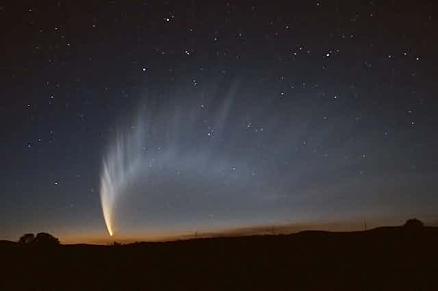 A photo showing a comet in the sky over a fading sunset, with a large tail billowing out behind it.
