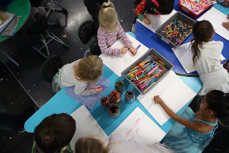 view from above children working with coloured pencils and crayons in school room.