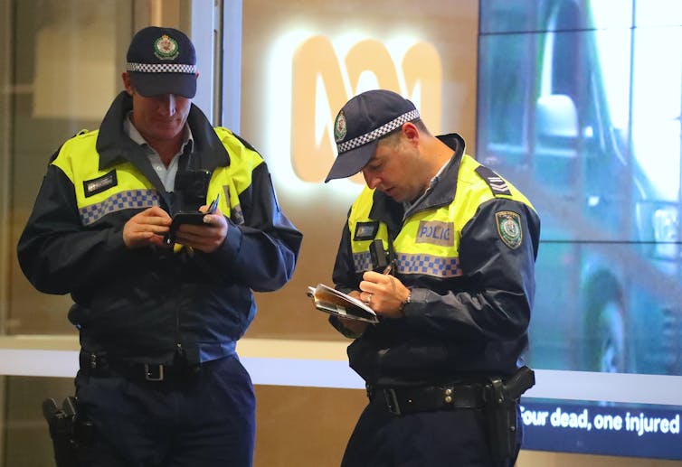 Two police officers stand in front of an ABC logo taking notes