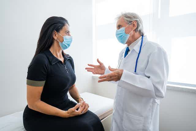 A doctor wearing a COVID mask consults with a female patient, also wearing a COVID mask.