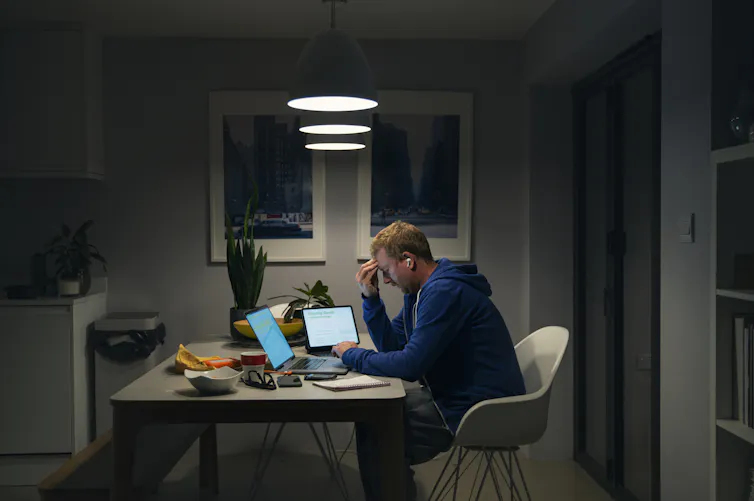 A man looks tired and frustrated while looking at screens and bills late at night
