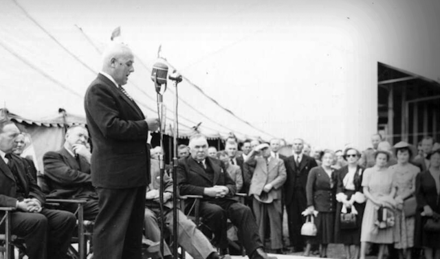 Black and white photo, a man stands on a dias.