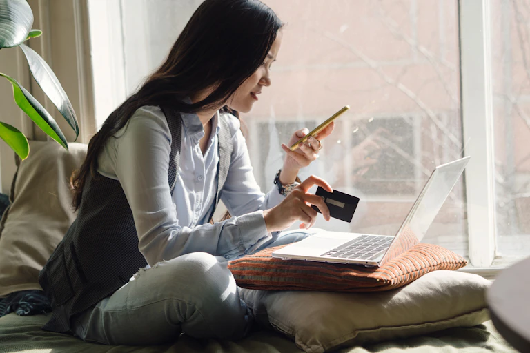 A woman sitting in a window seat with card, phone and laptop open