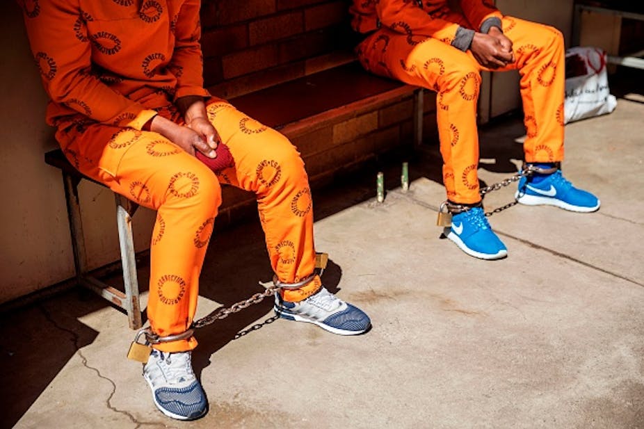 Two people in orange uniforms and leg chains, sitting on a bench.