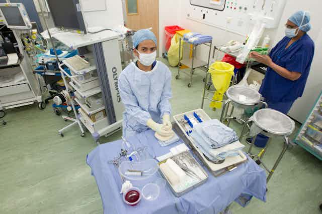 Two people in blue scrubs in an operating theatre.