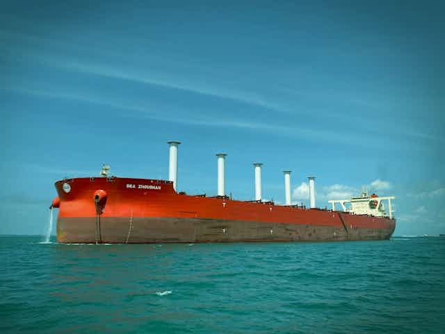 A red cargo ship with five white cylinders rising out of the deck.
