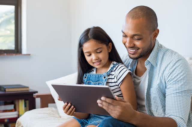 Father and daughter sit together looking at a tablet