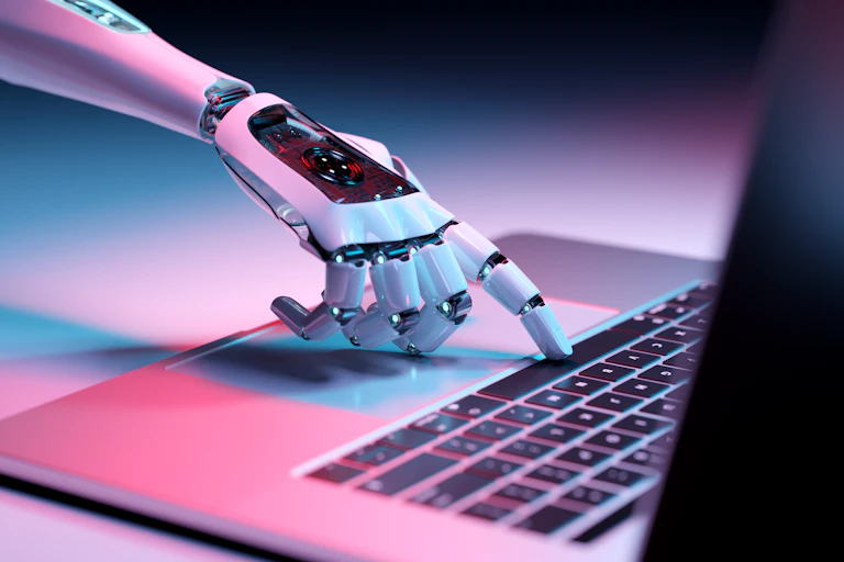 The index finger of a robotic hand hits the spacebar on a laptop computer.