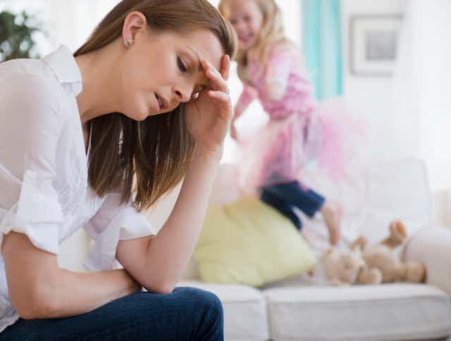Mom looking stressed out with child jumping on sofa in background