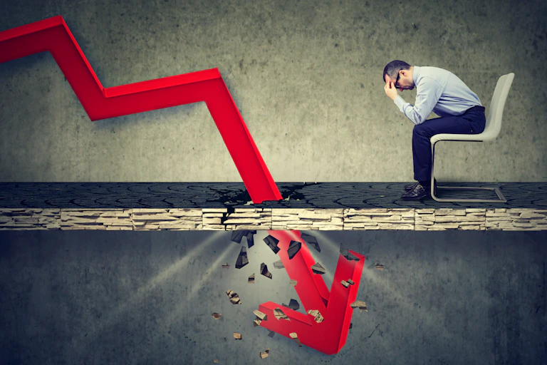 Illustration of a depressed businessman seated in front of a giant downward arrow