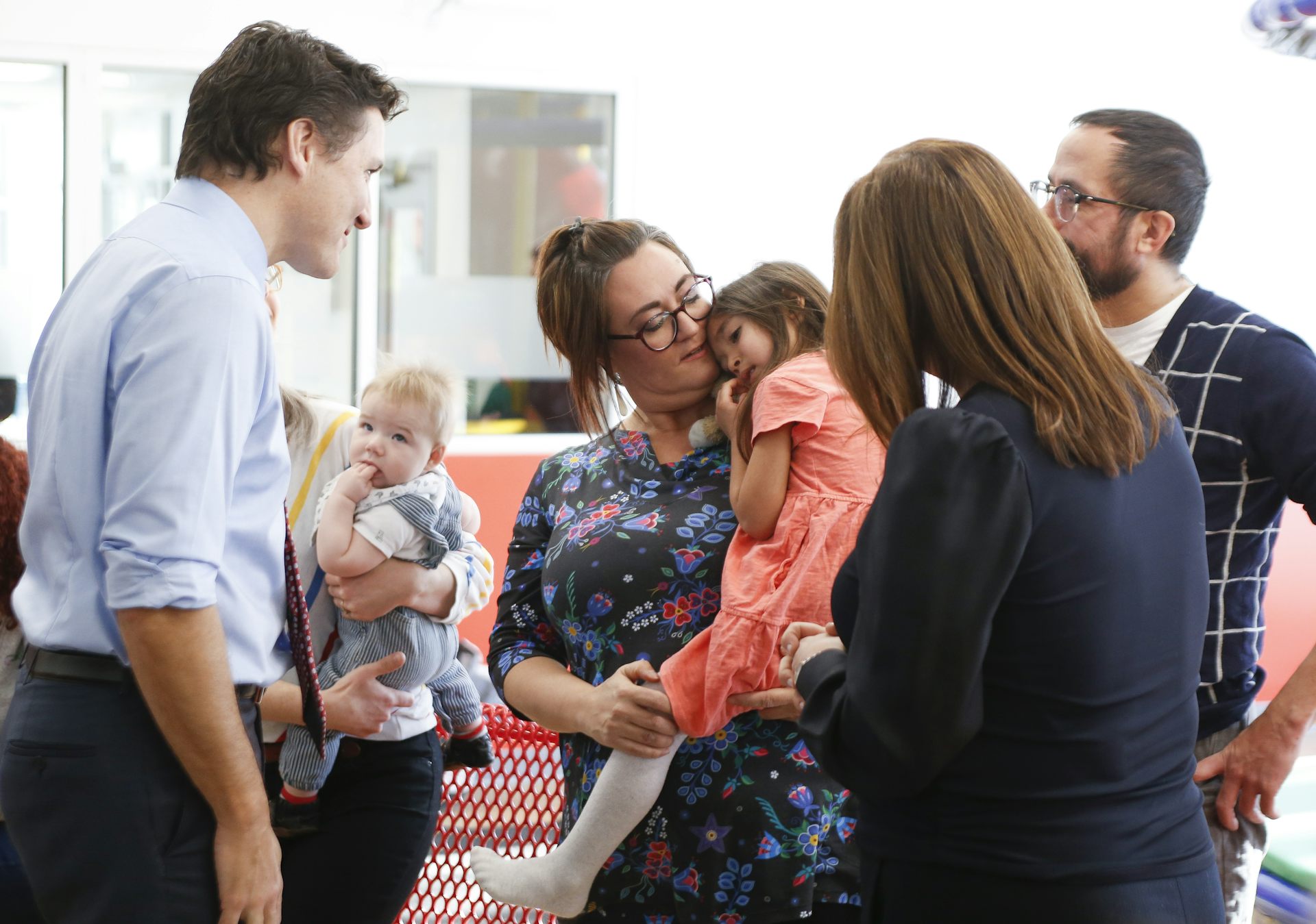 A dark-haired man talks to a woman and a shy girl in a peach-coloured dress.