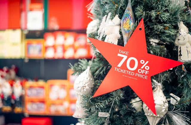 A star-shaped ornament that reads "Take 70% off ticketed price" is shown hanging from a Christmas tree at a Macy's department store.