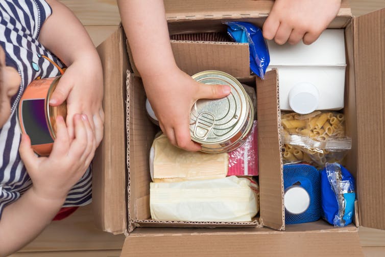 Young kids putting canned and dry food items in a box.
