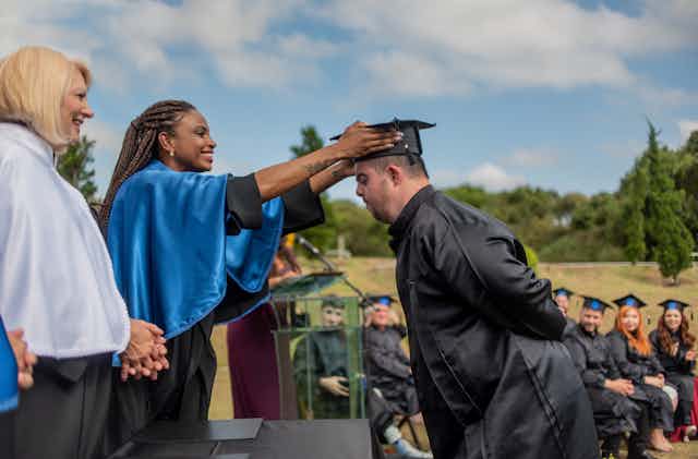 A woman adjusts the black graduation cap of a student at a graduation ceremony.