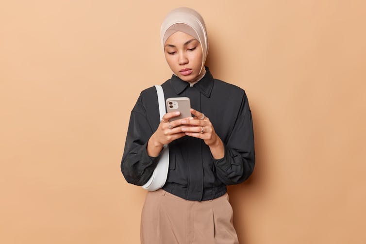 A woman in a hijab looks at her phone.