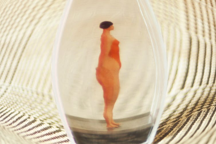 a woman in a red bathing suit with a black bob haircut seen through a distorted lens