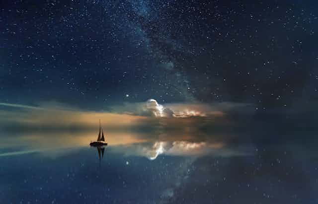 Un barco se desliza sobre un mar de aceite reflejando el cielo estrellado