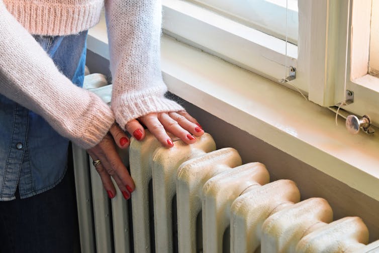 A woman's hands pressed against a radiator.
