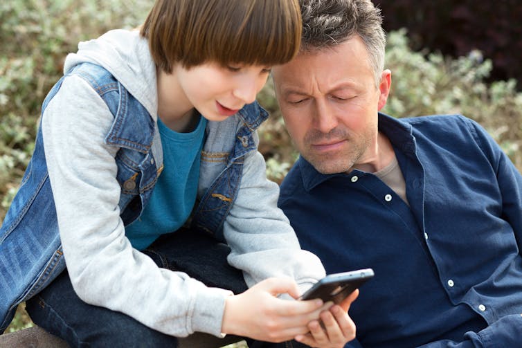 Un père et son fils regardent un téléphone portable.