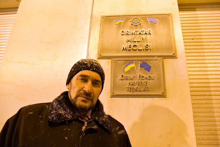 A man wearing a hat stands in front of the building, closed down by the Russian occupation of Crimea.