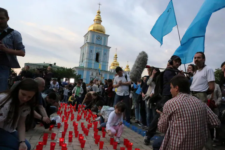 A group of children and adults light lines of red candles in front of an ornate church.