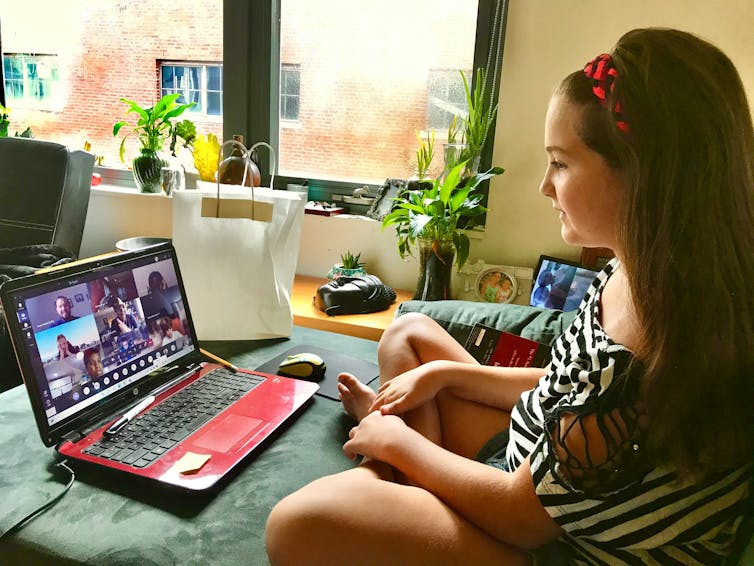 Girls sits on bed while taking part in video meeting on laptop