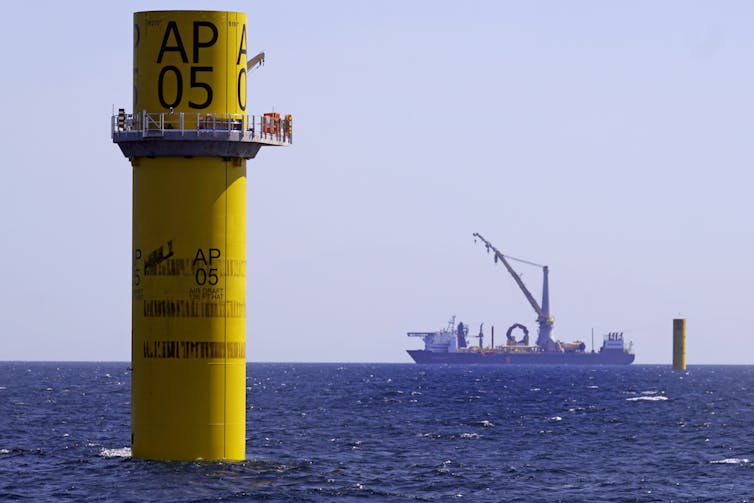 The foundation of an offshore wind turbine tower without the top yet, and a construction crane and another tower in the background.