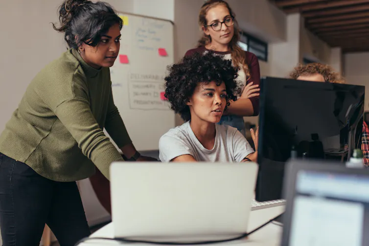 An ethnically diverse group of people have a conversation while looking at a computer screen.