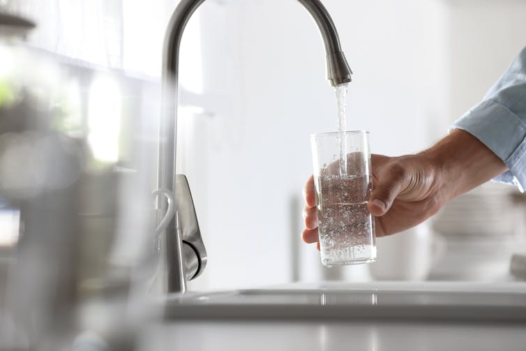 A hand holds a glass under the tap, filling it with water.