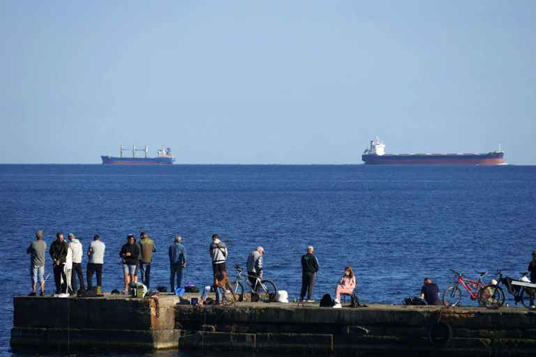 People stand on the harbour arm in Odesa, watching ships arrive.