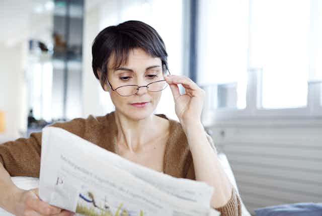 Woman with glasses reading newspaper.