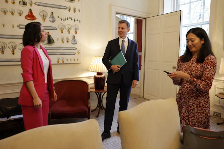 Jeremy Hunt holding autumn statement document, talking to two female colleagues.