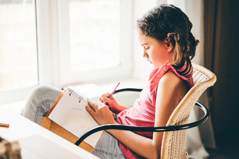 Girl sat in chair writing in notebook