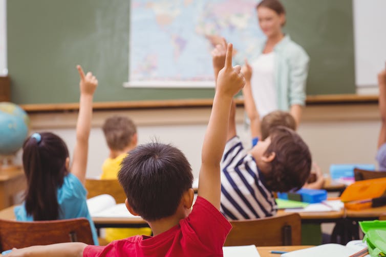Children putting hands up to answer teacher's question