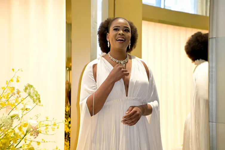 A woman in an Afro and flowing white dress raises her hand as she sings.