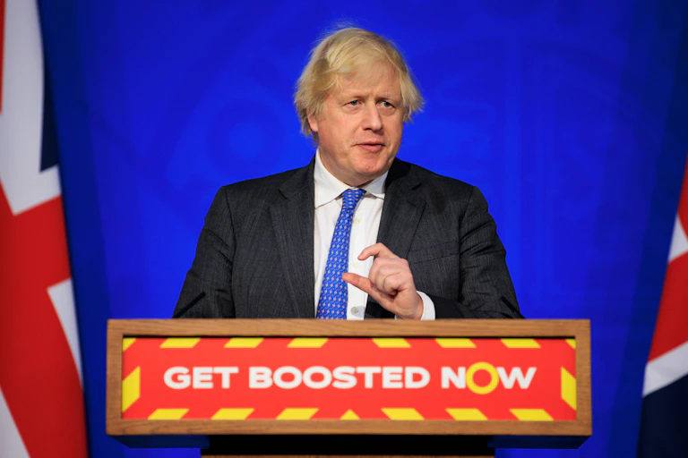 Boris Johnson speaking at a podium that reads 'get boosted now' during a coronavirus update