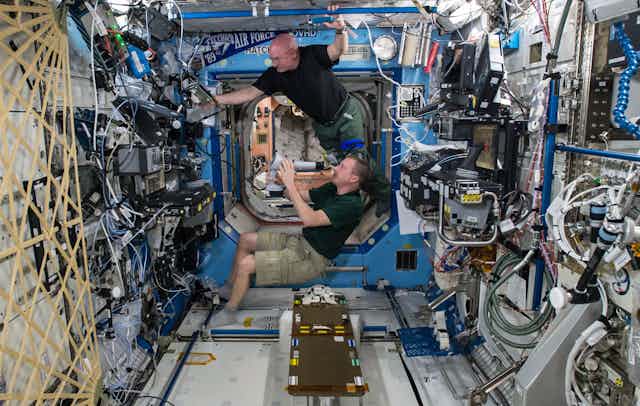 Dois astronautas trabalham num laboratório em gravidade zero, a bordo de uma estação espacial