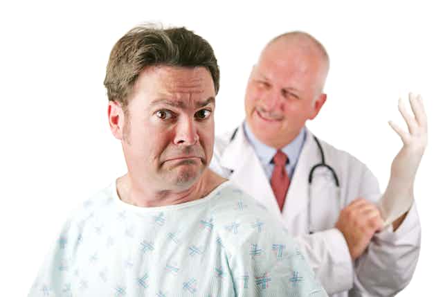 A man looking nervous with a doctor in the background putting on a latex glove