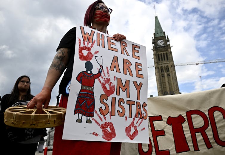 A woman seen with sign 'where are my sistas' printed with red hand marks.
