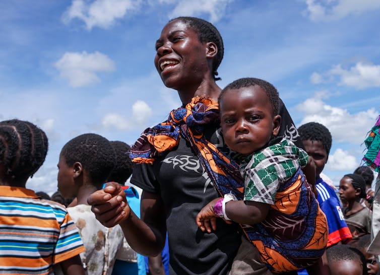 A baby holds on to his mother and looks at the camera in Liliachi, Zambia.