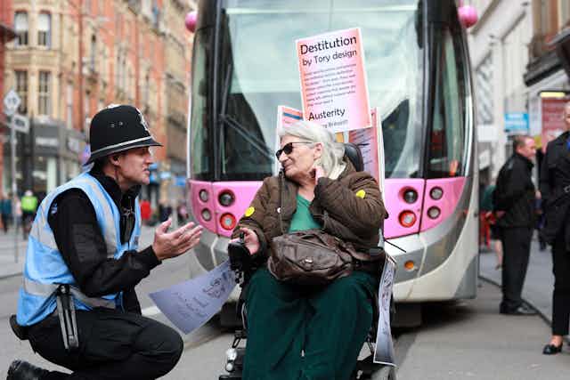 A pink bus behind a bobby in a blue vest and a female protestor in sunglasses. 