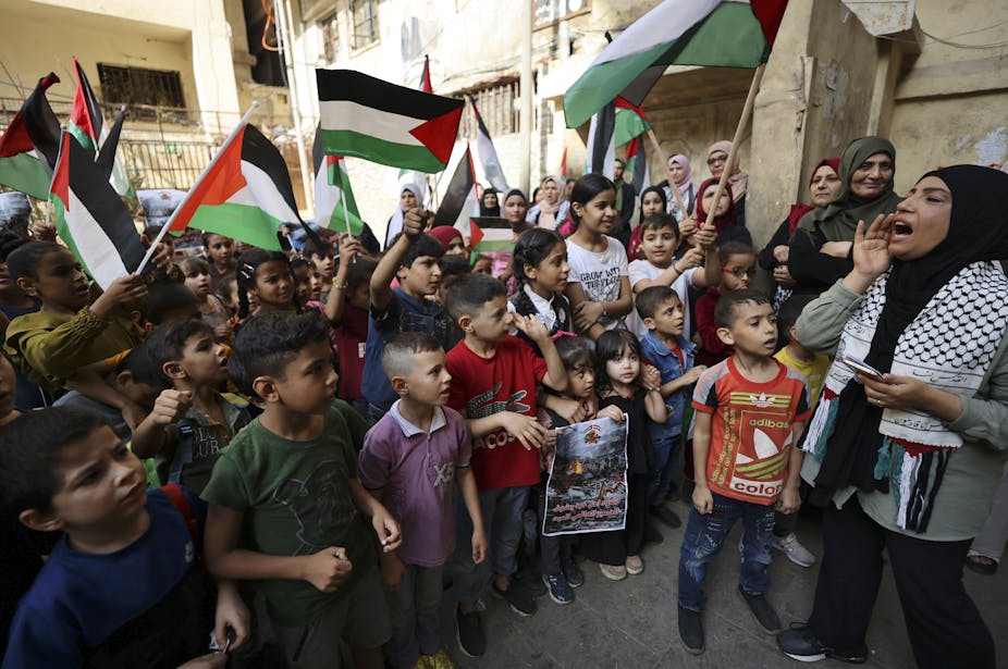 Une femme crie quelque chose devant des enfants portant des drapeaux palestiniens